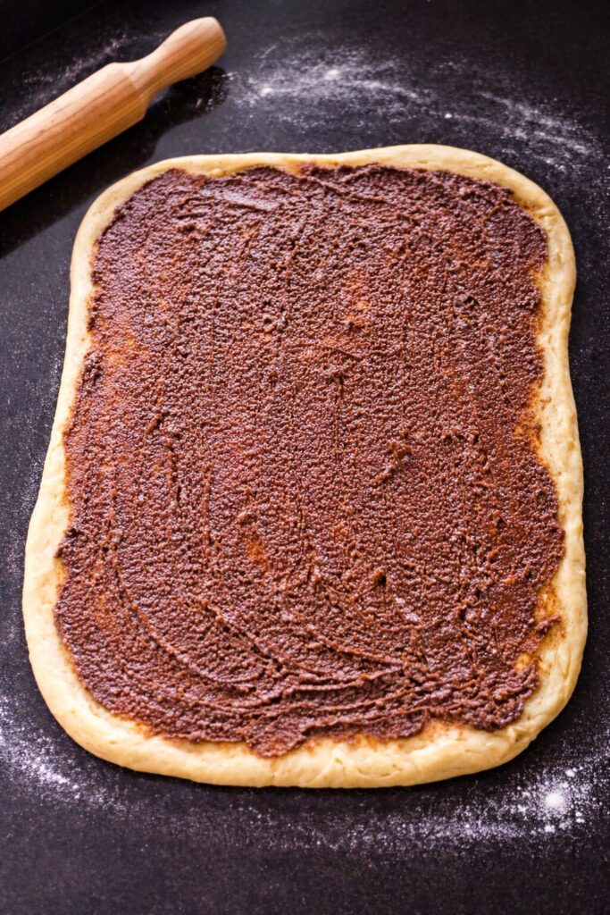 Masa de pistacho estirada con relleno de cacao untado, lista para enrollar.